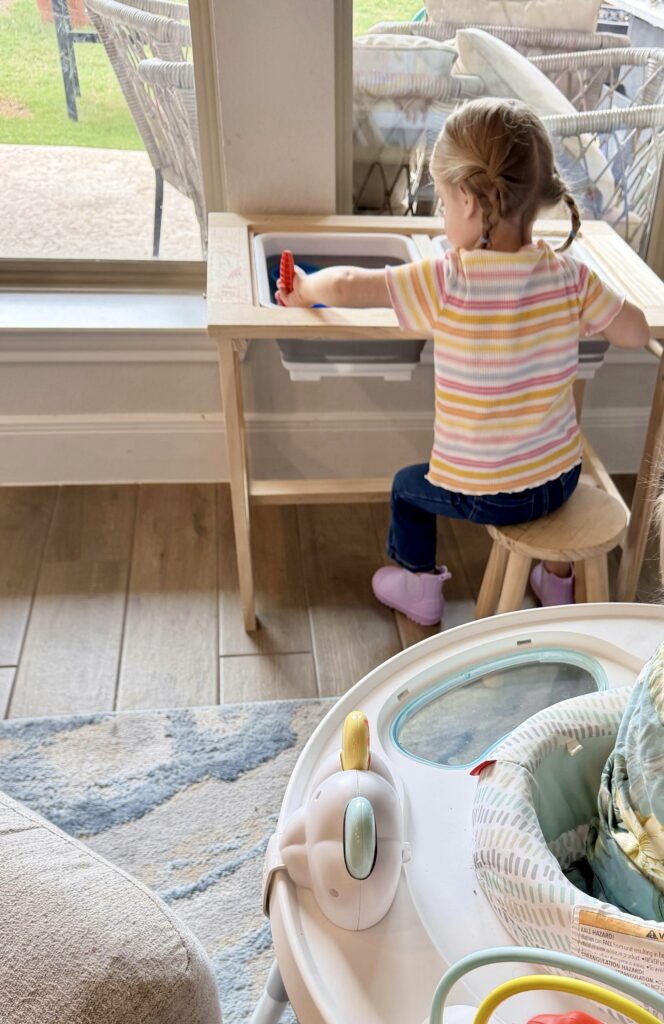 Toddler playing independently at a sensory table in a bright play area at home