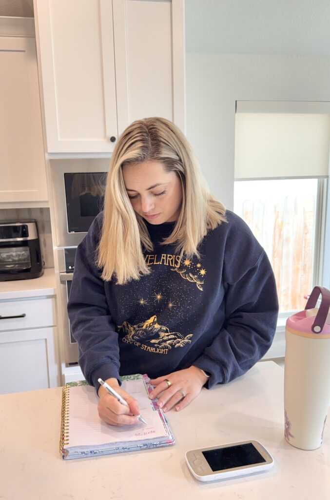 Stay at home mom writing in a planner at the kitchen counter while preparing for the week